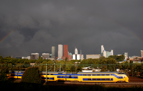 Regenboog, trein en skyline Den Haag